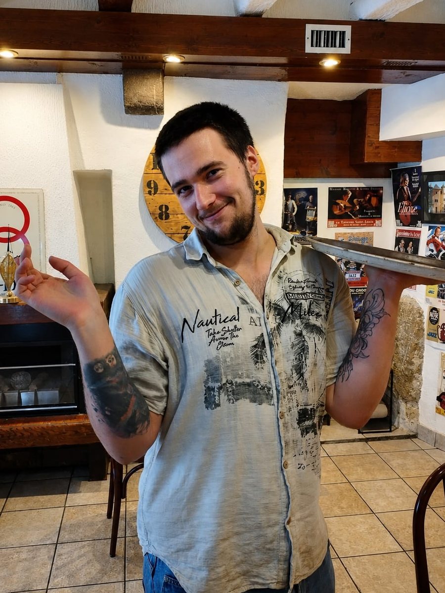 Alex, son plateau sur l'épaule, dans la salle de la taverne
